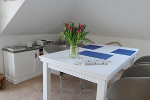 Un comedor con una mesa blanca, individuales azules y un jarrón con flores rosadas.