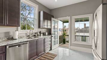 A modern kitchen with dark cabinets, a stainless steel refrigerator, and a large window.