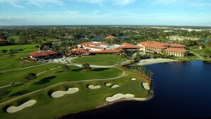 Um campo de golfe com um amplo complexo de edifícios, incluindo um clube da casa e vários quartos para hóspedes, próximo a um lago.