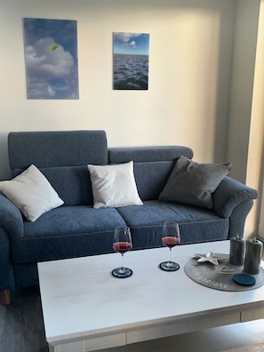A modern living room with a blue sofa, two white cushions, and a white coffee table with two wine glasses and candles. - 50.2.S Waterkant - Modern, high-quality vacation apartment, sauna, large balcony, (Wangerland)