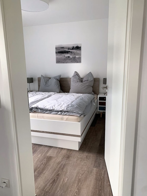 A modern bedroom with a bed, pillows, a bedside table, and a wall-mounted picture. - 50.2.S Waterkant - Modern, high-quality vacation apartment, sauna, large balcony, (Wangerland)