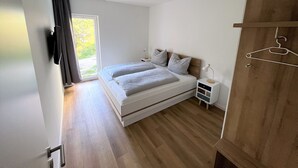 Un dormitorio con cama, mesitas de noche, armario y ventana con cortinas.