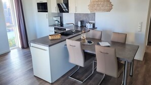 A modern kitchen with a central island, white cabinetry, and a dining area with a table and chairs. - 50.3.N Nordkoje - Modern, high-quality vacation apartment, sauna, large balcony, (Wangerland)