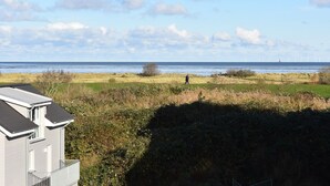 A coastal view with a grassy area, a person walking, and wind turbines in the distance. - 50.3.N Nordkoje - Modern, high-quality vacation apartment, sauna, large balcony, (Wangerland)