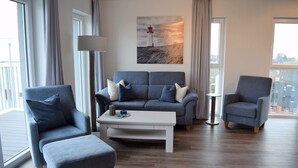 Ein modernes Wohnzimmer mit einer grauen Sofagarnitur, einem weißen Couchtisch und zwei Sesseln.