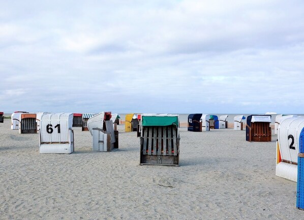 Cabañas de playa numeradas 61, 43 y 2, alineadas en una playa arenosa, con el mar al fondo.