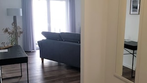 A modern living room with a dark grey sofa, a wooden coffee table, and a large mirror on the wall. - 49.4.M Ankerplatz - Modern, high-quality vacation apartment, sauna, large balcony, (Wangerland)