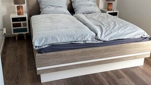 A modern bedroom with a wooden bed frame, two bedside tables with lamps, and a small nightstand with drawers. - 49.4.M Ankerplatz - Modern, high-quality vacation apartment, sauna, large balcony, (Wangerland)