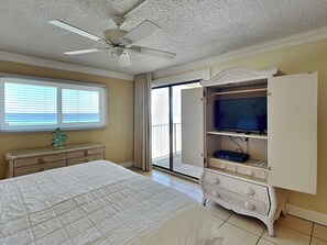 Ein Schlafzimmer mit Bett, Deckenventilator, Fernseher auf einem Schrank und Meerblick durch ein Fenster.