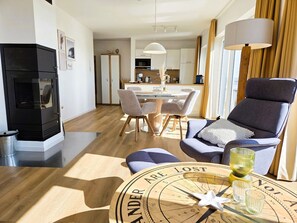 A modern living room with a black wood-burning stove, a dining area with a white table and chairs, and a large round coffee table with a compass design.