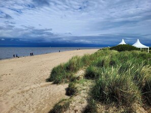 A beach with white tents and people walking along the shore.