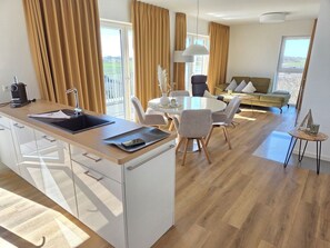 Een moderne keuken met een centraal eiland, een eethoek met stoelen, een bank en uitzicht op de omgeving.