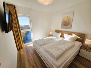 Habitación de hotel con una cama grande, televisión, ventana con cortinas, mesita de noche y una obra de arte en la pared.