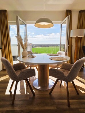 Un comedor con una mesa redonda, cuatro sillas, una lámpara colgante y ventanas amplias con vistas a un campo verde.
