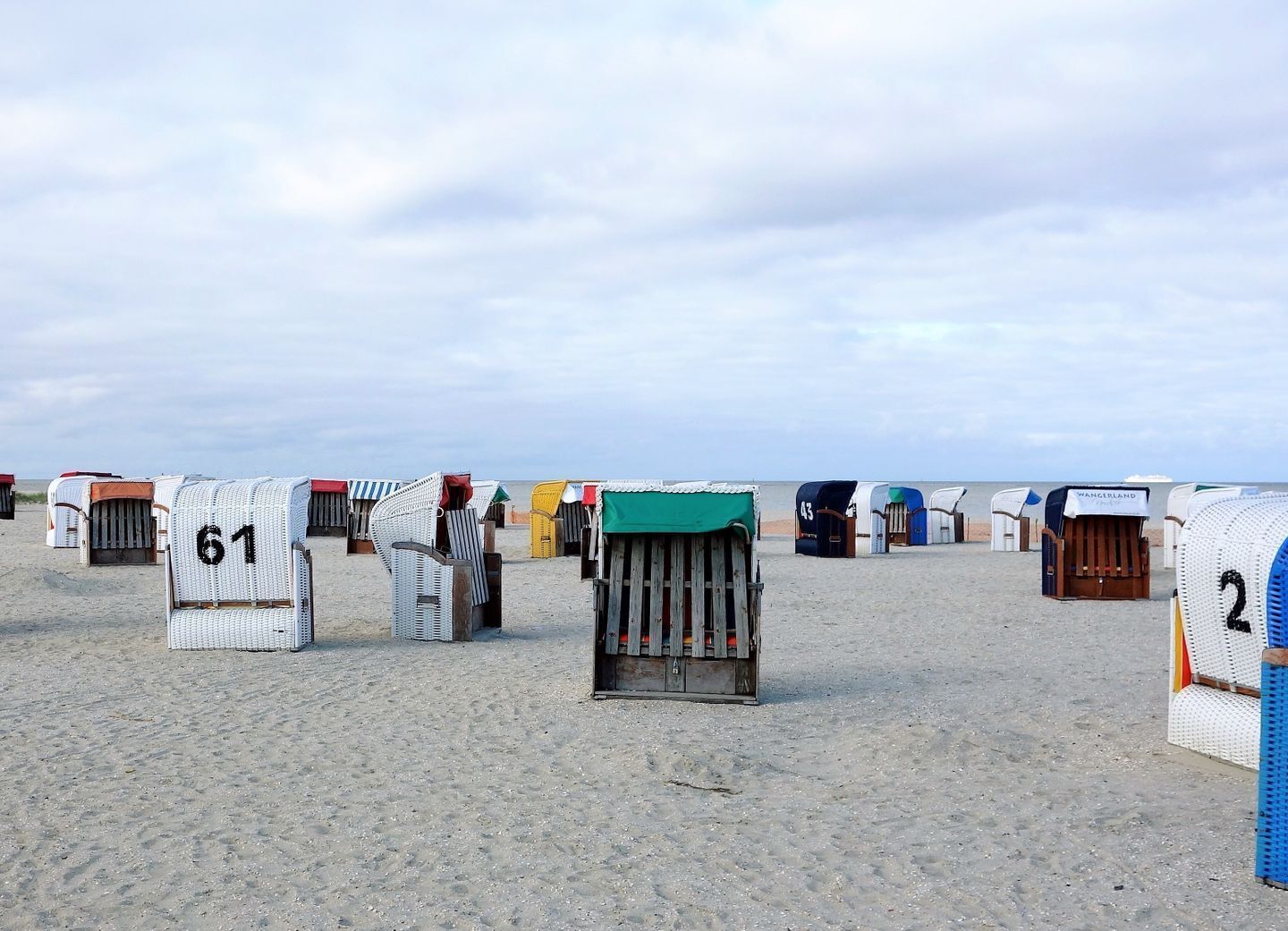 Beach huts numbered 61, 43, and 2, arranged in a row on a sandy beach with the sea in the background.