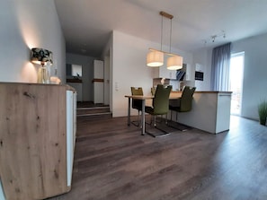 Una cucina moderna con zona pranzo, pavimento in legno e luci a sospensione.