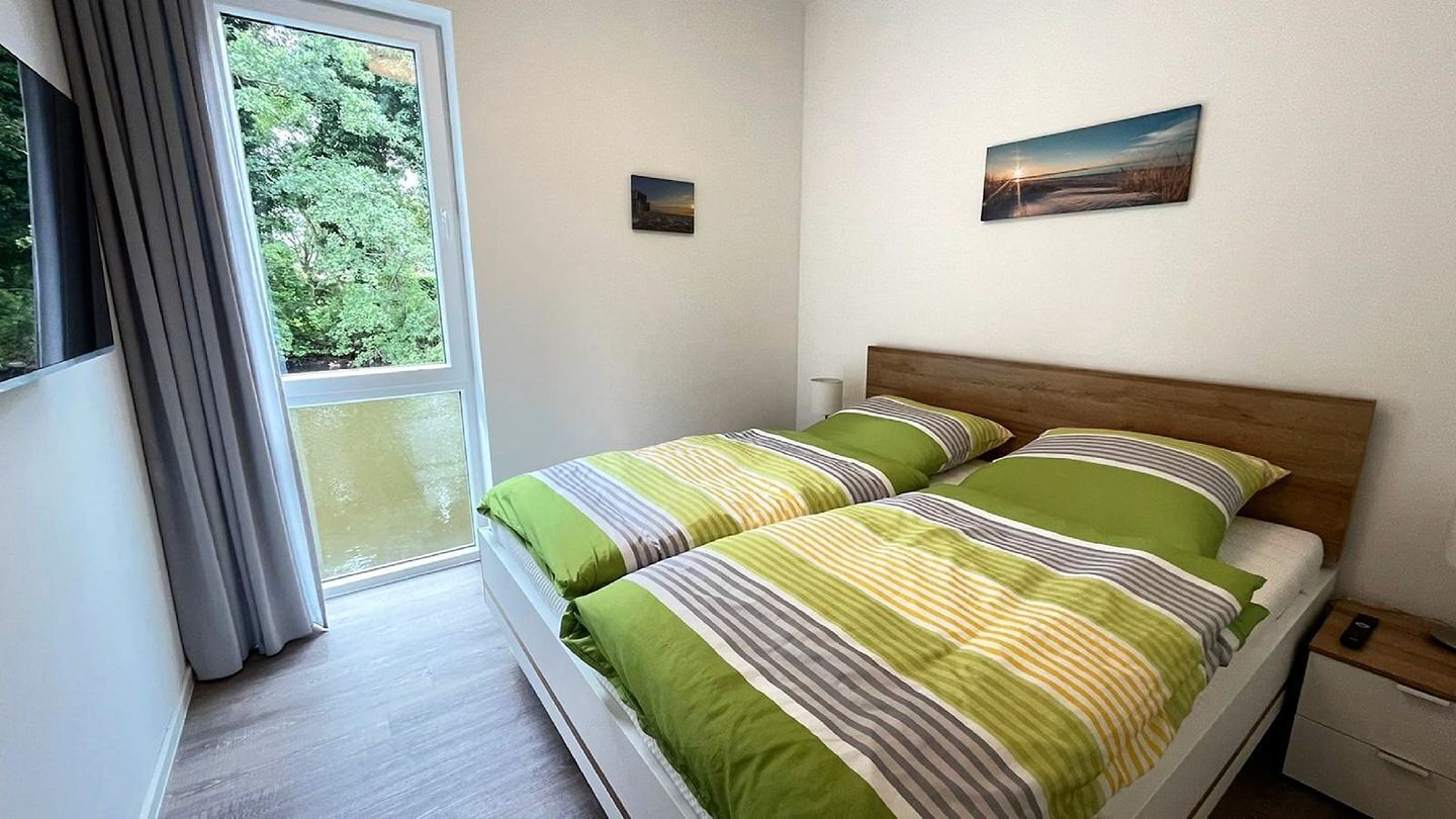 Une chambre à coucher comprenant un lit, une table de chevet, une fenêtre avec des rideaux et deux tableaux accrochés au mur.