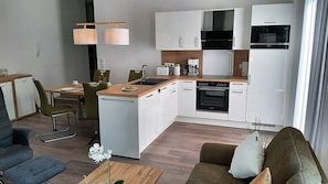 Una cucina moderna con mobili bianchi, forno a incasso e microonde. C'è un'area pranzo con tavolo e sedie, e un divano nella zona living.