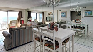 Ein großzügiger Wohnbereich mit Sofa, Esstisch und Stühlen, ein großer Spiegel der den Raum widerspiegelt und Meerblick durch große Fenster.