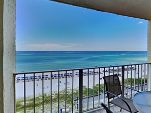 Een balkon met uitzicht op het strand, inclusief parasols en ligstoelen.