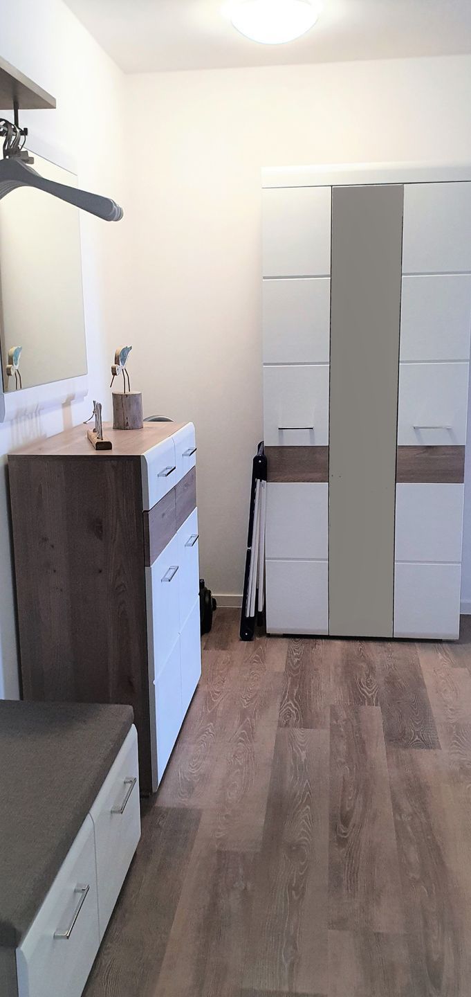A compact bedroom with a wooden dresser, a white wardrobe, and a mirror on the wall.