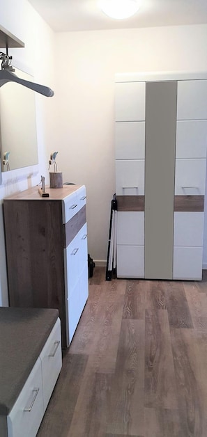 Ett litet sovrum med en byrå i trä, en vit garderob och en spegel på väggen.