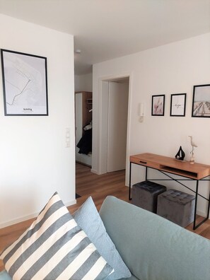Un salon moderne avec un canapé, des poufs, un bureau en bois et des œuvres d’art encadrées accrochées aux murs.