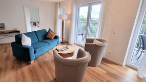 Un salon moderne avec un canapé bleu, une table basse ronde et un balcon doté d’une balustrade.