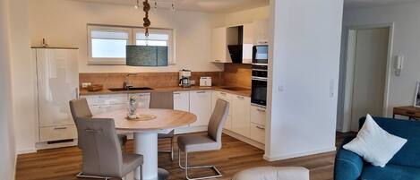 A modern kitchen with white cabinets, a wooden dining table, and a blue sofa in the living area.