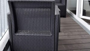 Un balcón con muebles de mimbre y un florero con plantas secas.