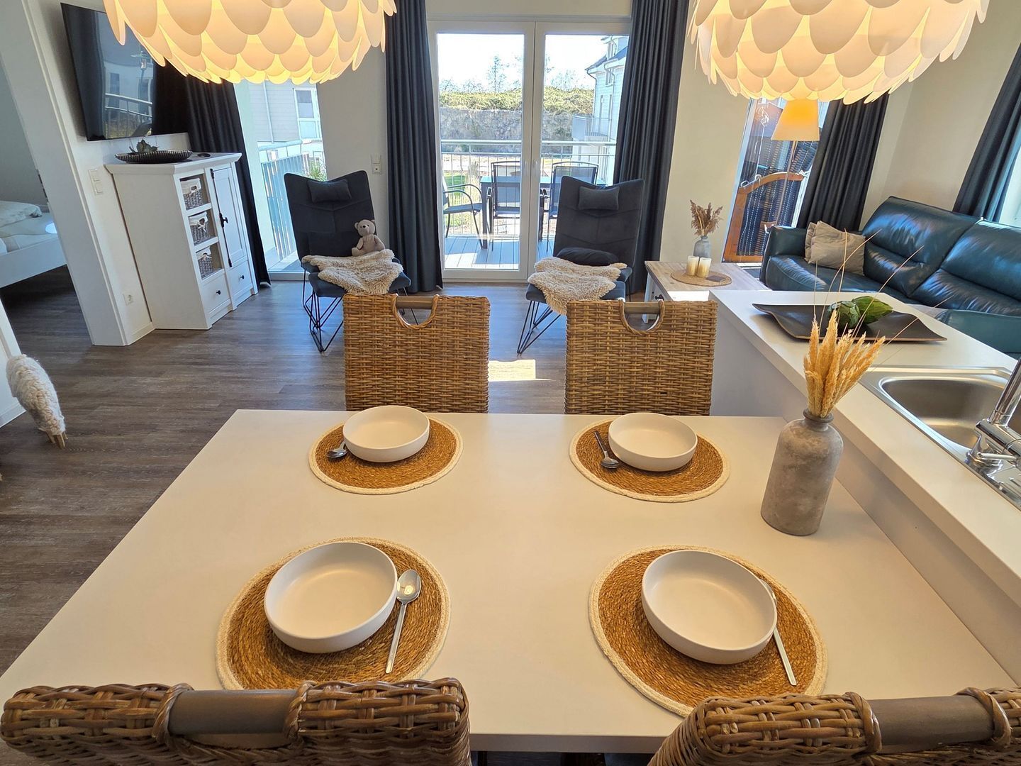 A modern dining area with a white table set for four, surrounded by wicker chairs and a wicker basket.