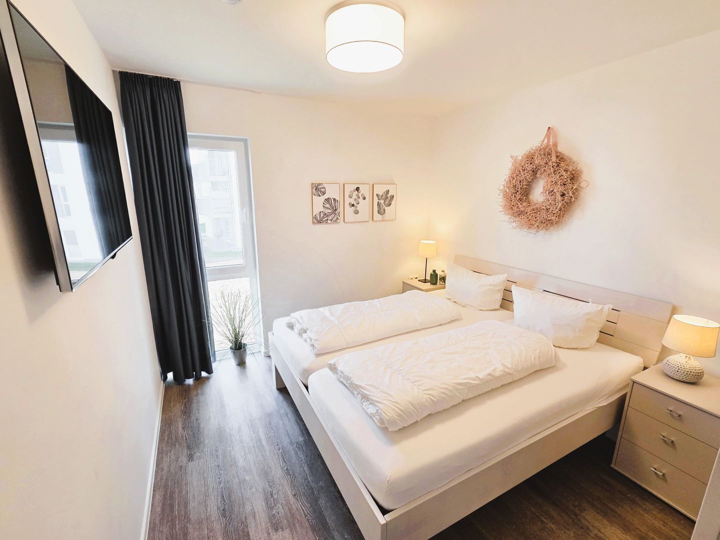 A hotel room with a large bed, bedside tables, a TV, and a window with curtains.