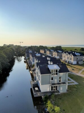 A residential area with modern houses along a canal, featuring a mix of single and double-story buildings with flat roofs and large windows. - 47.5.S Waterkant - Cozy, high-quality vacation apartment, own sauna, south-facing, (Wangerland)