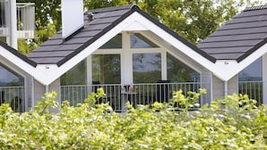 Et moderne hus med skråt tag, store vinduer og en balkon med gelænder.