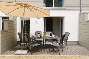 A patio with a table set for two, surrounded by chairs, under a large umbrella.