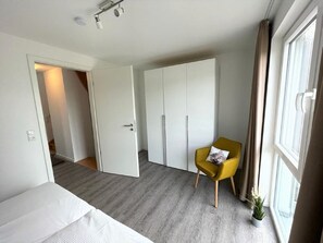 Ett modernt hotellrum med en säng, en gul fåtölj, en garderob och en krukväxt.