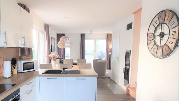 A modern kitchen with a central island, white cabinetry, and a large wall clock. - House No. 22, Ferienhaus Deichgraf - Modern vacation home, fireplace, sauna, south (Wangerland)