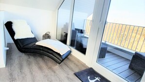 A balcony with a black chair, a small table, and a wicker chair. - House No. 22, Ferienhaus Deichgraf - Modern vacation home, fireplace, sauna, south (Wangerland)