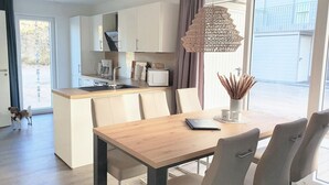 A modern kitchen with white cabinets, a wooden island, and a dining area with a table and chairs. - House No. 22, Ferienhaus Deichgraf - Modern vacation home, fireplace, sauna, south (Wangerland)