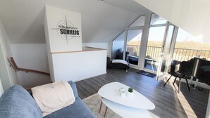 A modern living room with a sofa, a coffee table, and a balcony with a view. - House No. 22, Ferienhaus Deichgraf - Modern vacation home, fireplace, sauna, south (Wangerland)