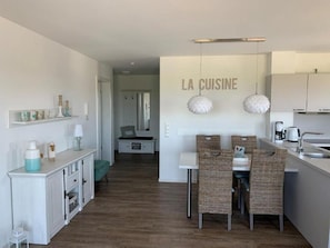 Une cuisine moderne avec un coin repas, des meubles blancs et une enseigne indiquant « LA CUISINE ».