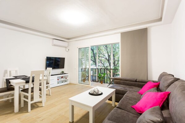 A modern living room with a white sofa, a dining table, and a TV. - Rentalsevilla Spacious Apartment in Alfalfa (Sevilla)
