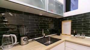 Una cocina moderna con salpicadero de baldosas negras, un lavamanos de acero inoxidable, una cafetera y una licuadora.