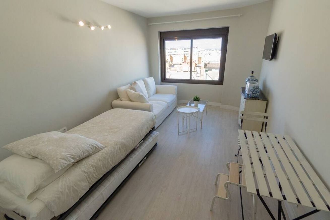A compact, well-lit room with a bed, a sofa, a small table, and a window offering a city view.