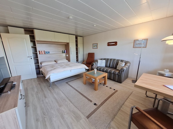 Et kompakt værelse med en seng, en stribet sofa, et lille bord og et skrivebord.