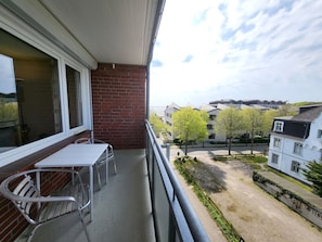 En balkon med et bord og stole, en murstensvæg og udsigt over et boligområde med huse og træer.