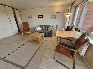 En moderne stue med sofa, sofabord, spisebord med stole, reol og radiator.