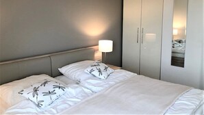 Quarto de hotel com cama, mesa de cabeceira, abajur e guarda-roupa.