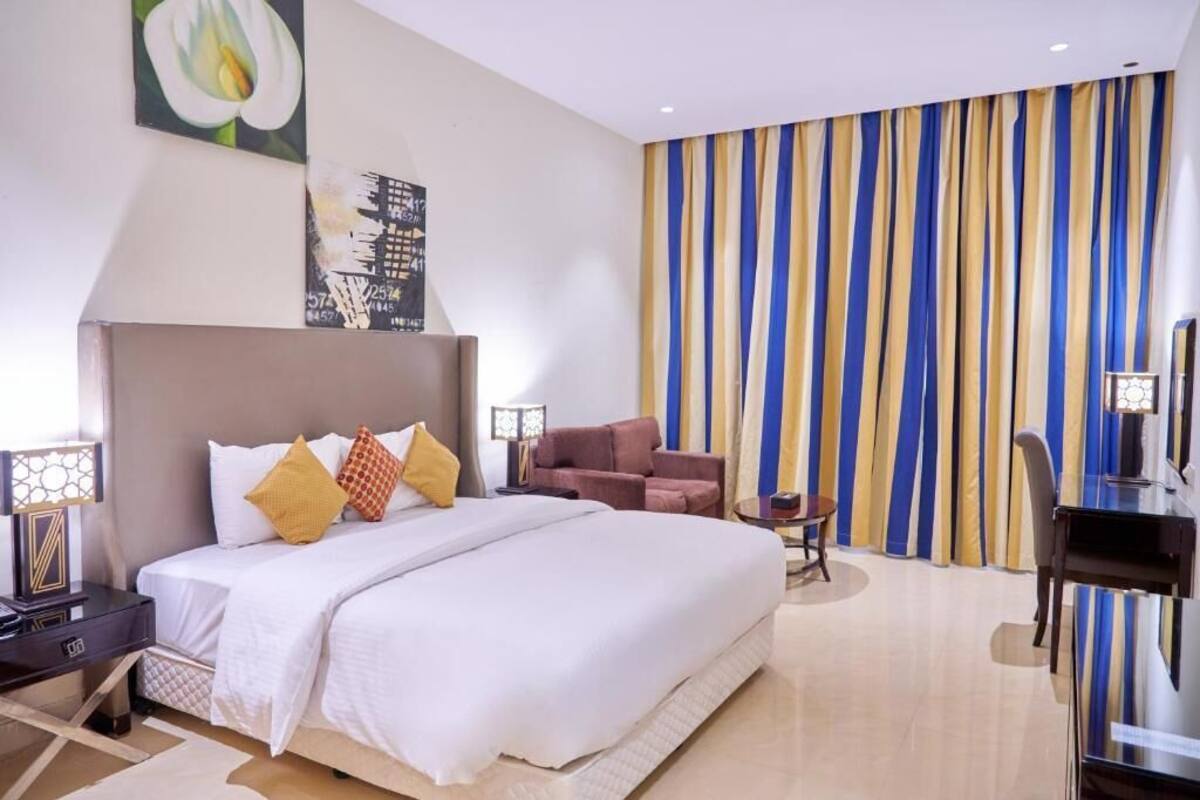 A modern hotel room with a large bed, a desk, a chair, and a TV.