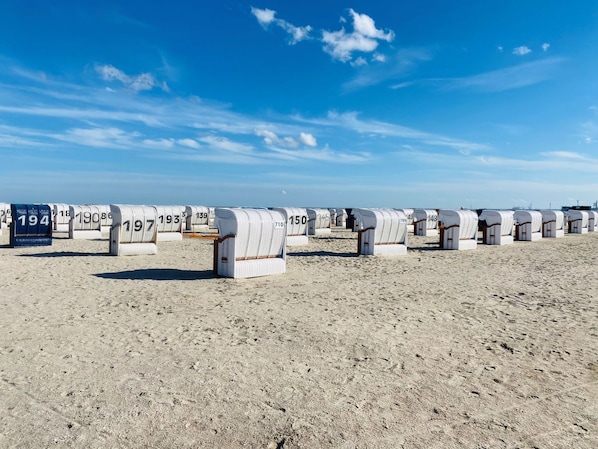 Rows of numbered beach huts on a sandy beach under a clear sky. - 47.3.M Seestern - Well-kept apartment with sea view, infrared cabin, large balcony (Wangerland)